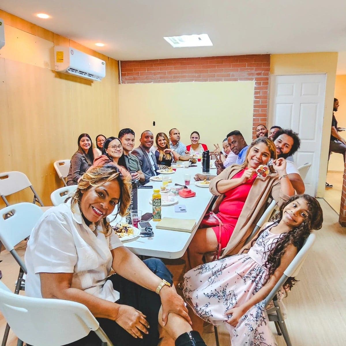La comunidad reunida en el salón, saludando a la cámara